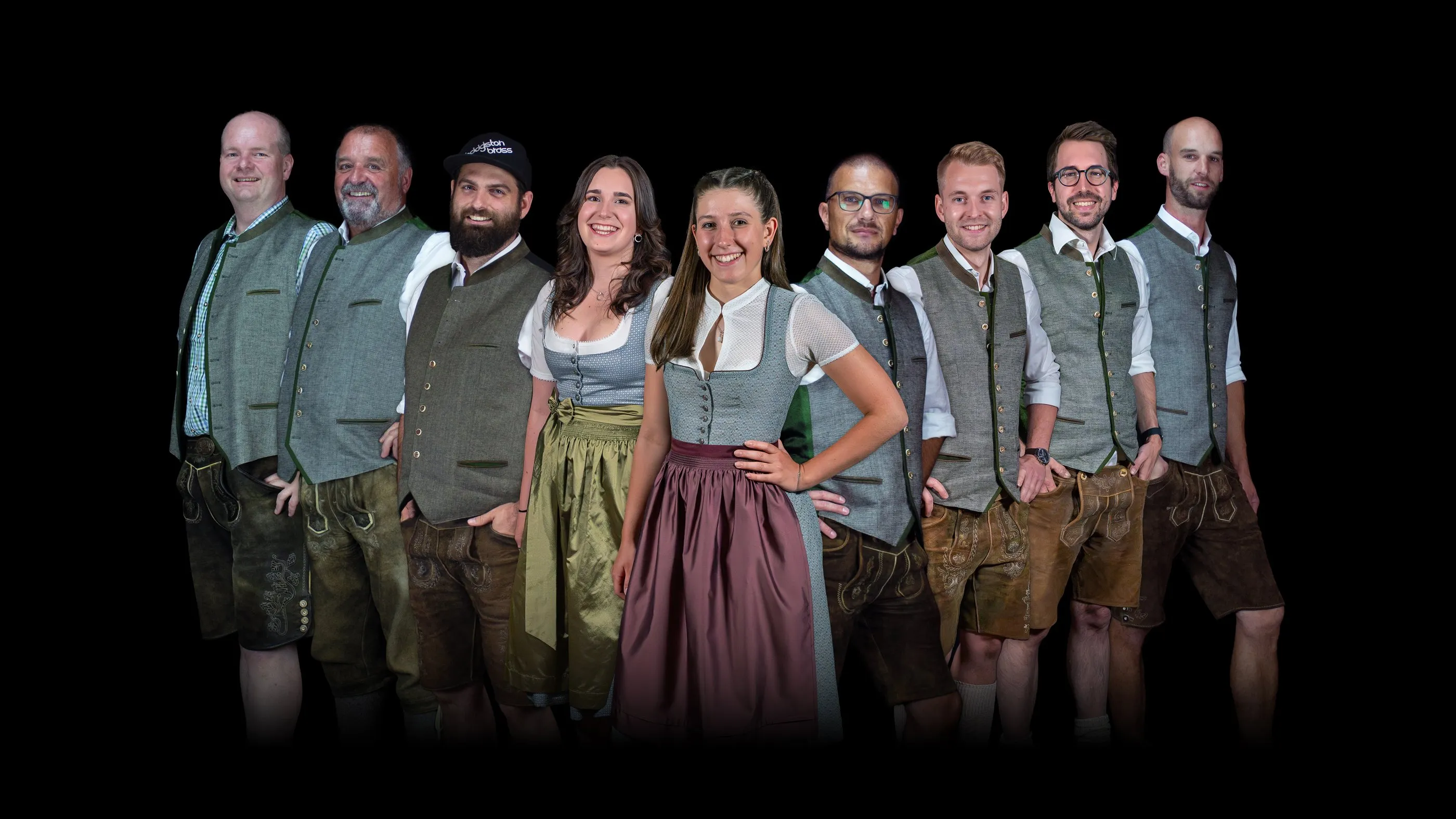 Die neun Mitglieder von Haagston Brass in Tracht vor schwarzem Hintergrund
